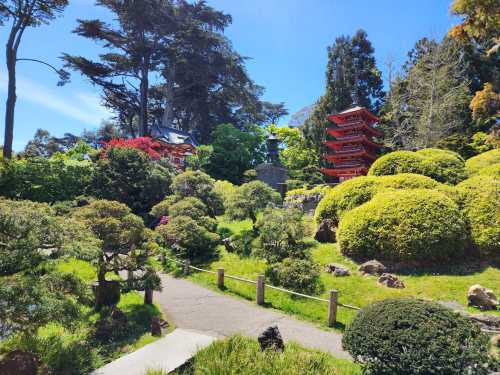 A serene garden with lush greenery, a winding path, and a red pagoda in the background under a clear blue sky.