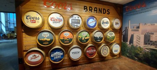 A wall display featuring various Coors beer brand logos on barrel-shaped signs.