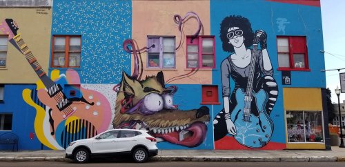 Colorful mural featuring guitars, a cartoonish wolf, and a musician with an electric guitar on a vibrant wall.