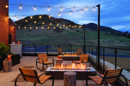 Cozy outdoor patio with string lights, fire pits, and mountain views at dusk.