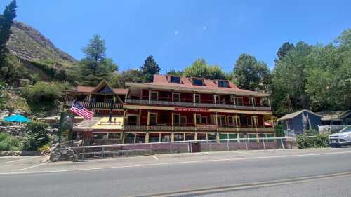 A charming multi-story building with a red roof, surrounded by trees, and an American flag in front, along a road.