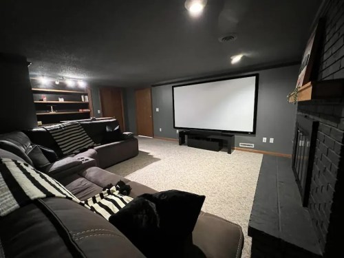 Cozy basement living room with a large screen, sectional sofa, and a fireplace, featuring dim lighting and a neutral color scheme.