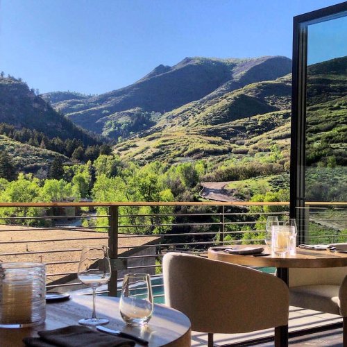 A scenic view of green mountains and blue sky from a dining area with a table set for a meal.