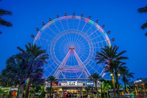 A colorful Ferris wheel at dusk, surrounded by palm trees and lively visitors at Icon Park.