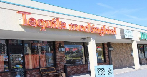 Sign for "Tequila Mockingbird" on a storefront, featuring bright orange letters against a light-colored building.