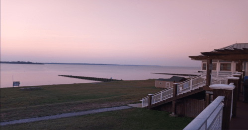 A serene waterfront view at dusk, featuring calm waters, a pier, and a building with a deck.