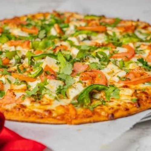 A freshly baked pizza topped with green peppers, tomatoes, onions, and herbs on a parchment-lined surface.