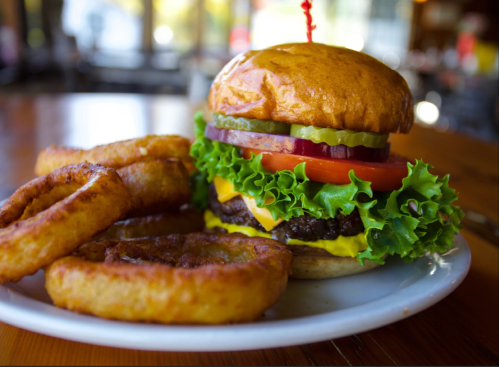 A juicy burger with lettuce, tomato, pickles, and cheese, served with crispy onion rings on a white plate.