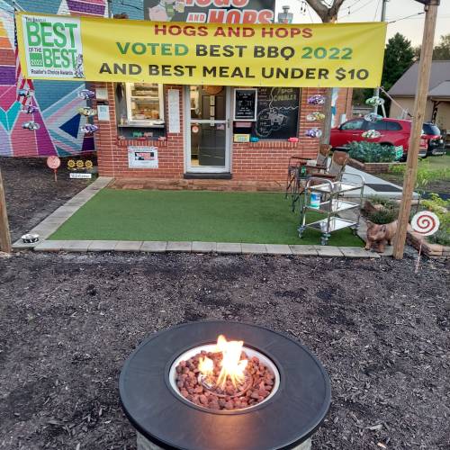 A cozy outdoor BBQ spot with a fire pit, sign announcing awards, and a colorful building in the background.