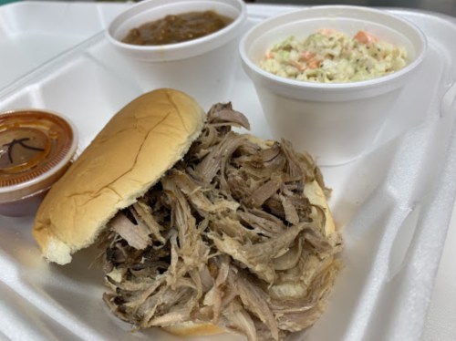 A plate featuring a pulled pork sandwich, coleslaw, and baked beans in separate containers.