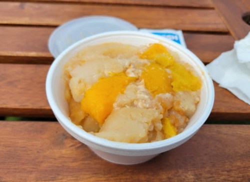 A cup of creamy dessert with chunks of yellow and orange fruit, placed on a wooden table.