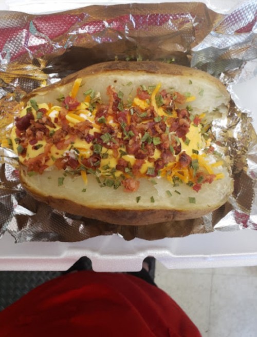A loaded baked potato topped with cheese, bacon bits, and green onions, served in foil.
