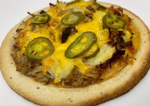 A close-up of a pizza topped with pulled pork, cheese, jalapeños, and pineapple on a golden crust.