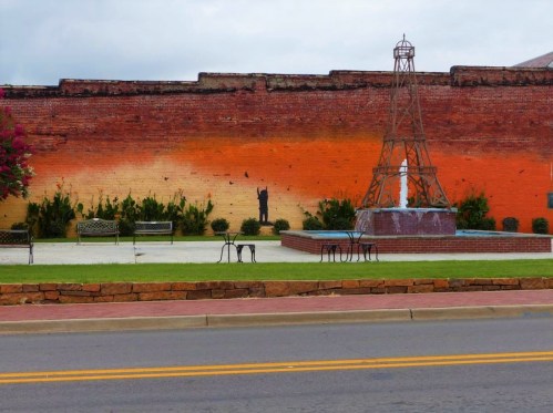 A vibrant mural on a brick wall features a silhouette against an orange gradient, with a fountain and benches in the foreground.