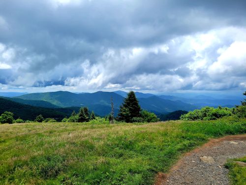 A scenic view of rolling green mountains under a cloudy sky, with a grassy foreground and a winding path.