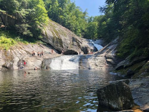 A scenic waterfall surrounded by lush greenery, with people swimming and enjoying the natural pool below.