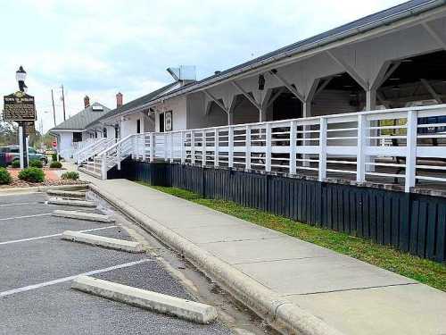 A white building with a covered porch and a ramp, surrounded by a parking lot and grassy area.