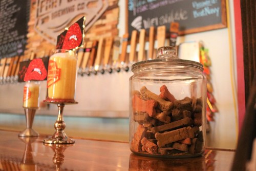 A glass jar filled with dog treats sits on a bar counter, with decorative candles and a beer tap backdrop.