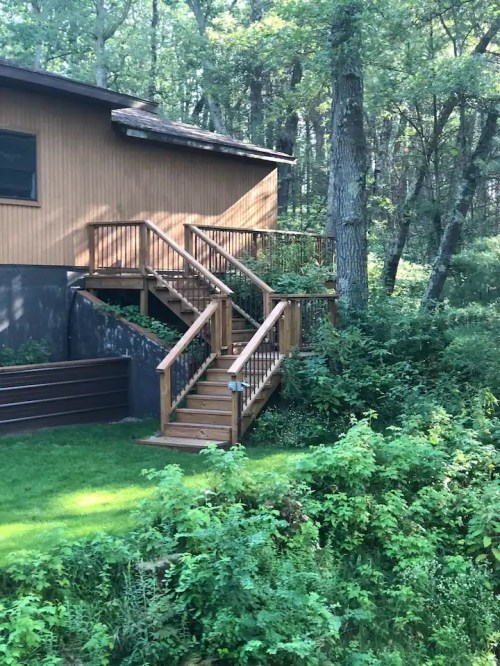 A wooden staircase leads up to a house surrounded by lush greenery and trees.