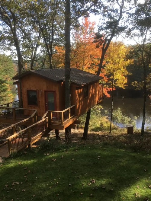 A cozy treehouse nestled among trees, overlooking a serene lake with autumn foliage in vibrant colors.