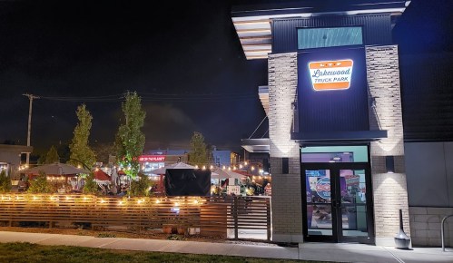 A vibrant night scene of Lakewood Truck Park, featuring food trucks and outdoor seating illuminated by string lights.