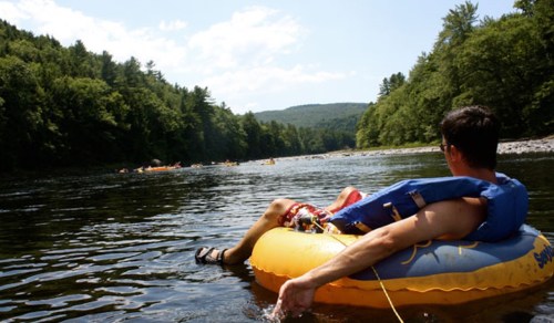 A person relaxes on an inflatable tube in a river, surrounded by trees and other tubers in the distance.