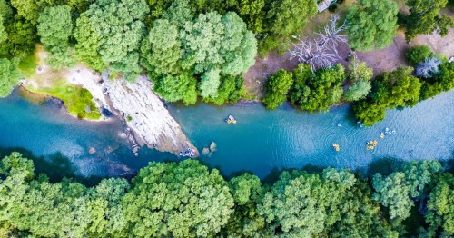 Aerial views of clear water and trees along the Guadalupe River tubing route, featuring small groups of people floating on inner tubes.