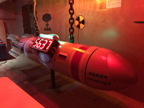 A large, cylindrical object with a digital timer, hanging in a dimly lit room with warning signs.