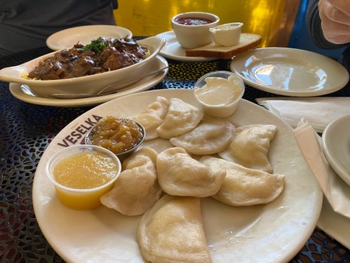 A plate of dumplings with sauces, alongside a bowl of meat and a slice of bread on a table.
