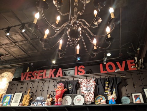 A cozy interior featuring a chandelier and a shelf with the words "VESSELKA IS LOVE," along with various decorations and memorabilia.