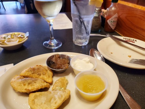 A plate with fried dumplings, sauces, and a glass of white wine on a table at a restaurant.