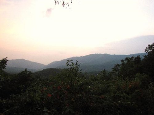 A serene landscape featuring rolling mountains under a soft, pastel sky at dusk, surrounded by lush greenery.