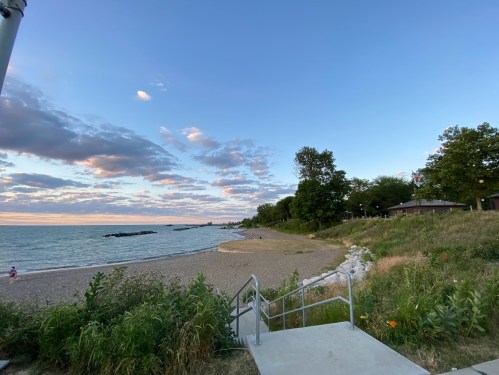 A serene beach scene at sunset, featuring a sandy shore, gentle waves, and lush greenery under a colorful sky.