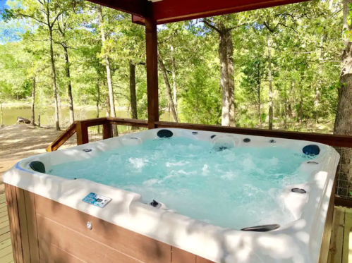 A hot tub with bubbling water, surrounded by trees and nature under a wooden gazebo.