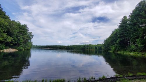 A serene lake surrounded by lush green trees under a partly cloudy sky, reflecting the landscape in calm waters.