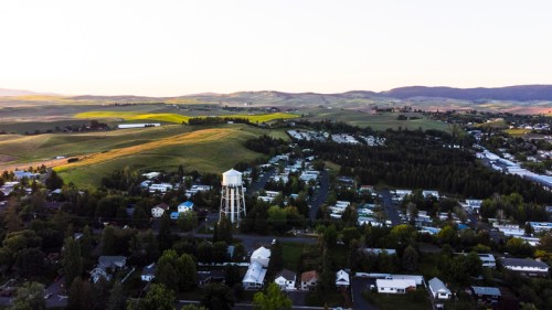 Aerial view of a rural town with rolling hills, a water tower, and residential areas under a clear sky.