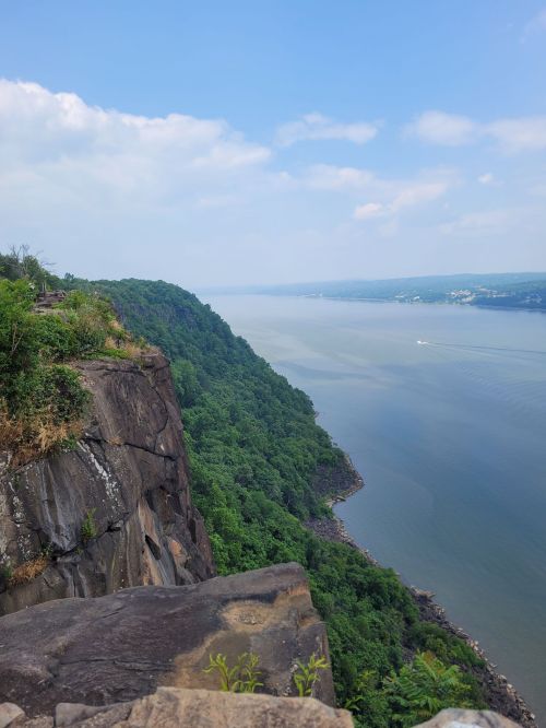 A scenic view of a river bordered by lush green hills and rocky cliffs under a clear blue sky.