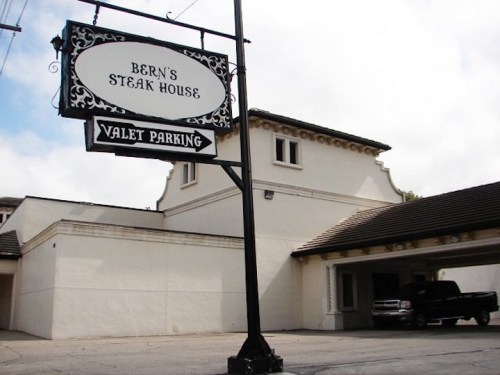 Sign for Bern's Steak House with valet parking, featuring a classic building in the background under a cloudy sky.