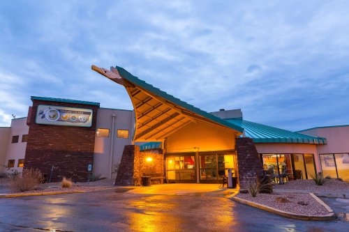 A modern building with a distinctive roof design, illuminated at dusk, surrounded by desert landscaping.