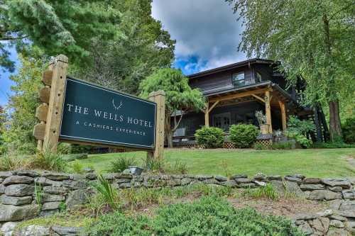 Sign for The Wells Hotel, surrounded by greenery and trees, with a rustic wooden building in the background.