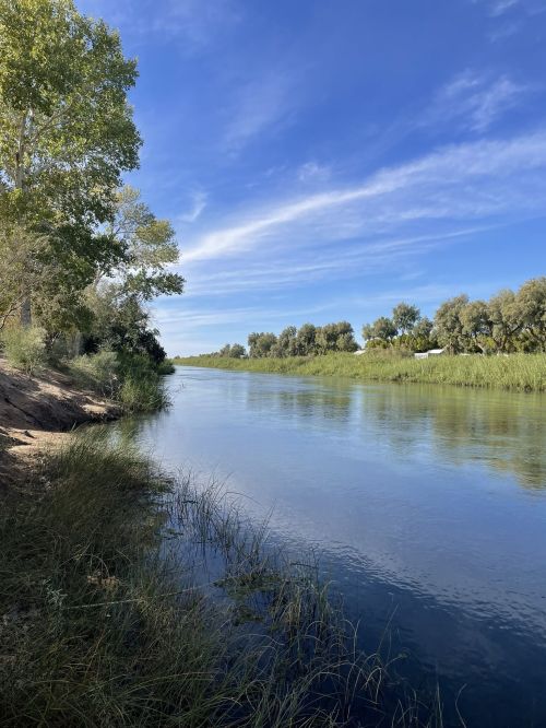 A serene river scene with lush greenery and a clear blue sky, reflecting calm waters and gentle shorelines.