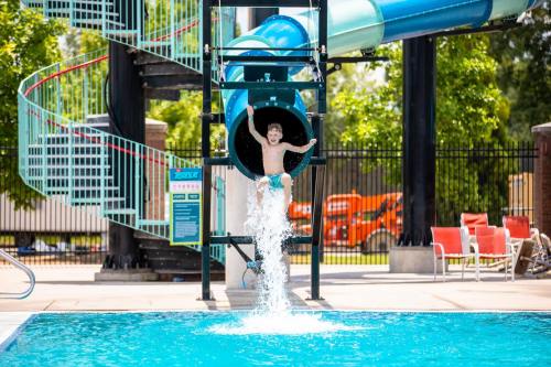A child joyfully splashes into a pool after sliding down a water slide on a sunny day.