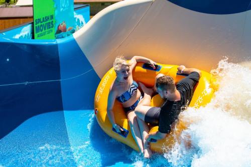 A woman and a man enjoy a water slide in an inflatable tube, splashing through the water.