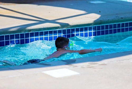 A young boy swims in a pool, wearing a snorkel and goggles, with water splashing around him.
