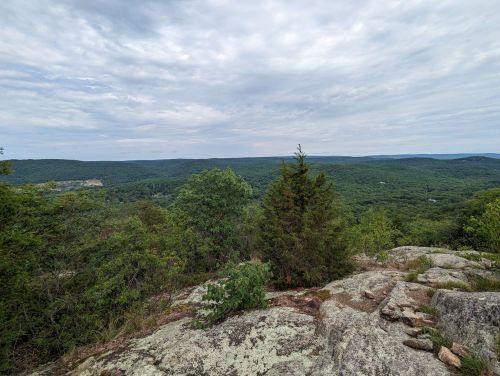 A scenic view from a rocky outcrop, showcasing lush green hills and a cloudy sky in the background.