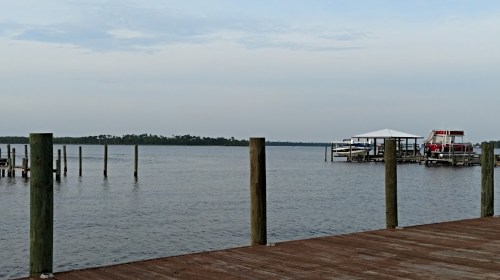 A calm waterfront scene with wooden posts, a dock, and a boat house under a cloudy sky.