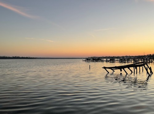 A serene sunset over calm waters, with silhouettes of wooden piers in the foreground.