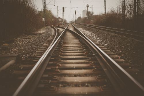 A close-up view of railway tracks converging in the distance, surrounded by sparse vegetation and signaling lights.