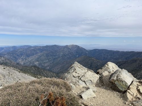 A panoramic view of rugged mountains under a cloudy sky, with rocky terrain in the foreground.