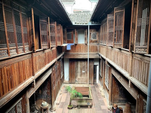 A traditional wooden courtyard with balconies, featuring a central stone well and potted plants.